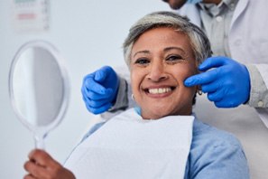 Woman smiling while holding handheld mirror at dentist's office