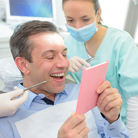 Man in the dental chair looking at his new smile in a mirror
