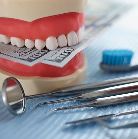 An artificial jaw mockup biting dollar bills set next to dental tools