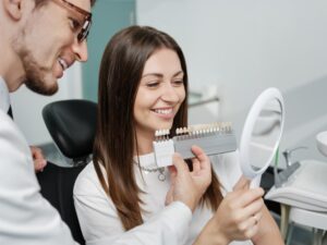 Dentist showing young lady patient different shades of veneers.